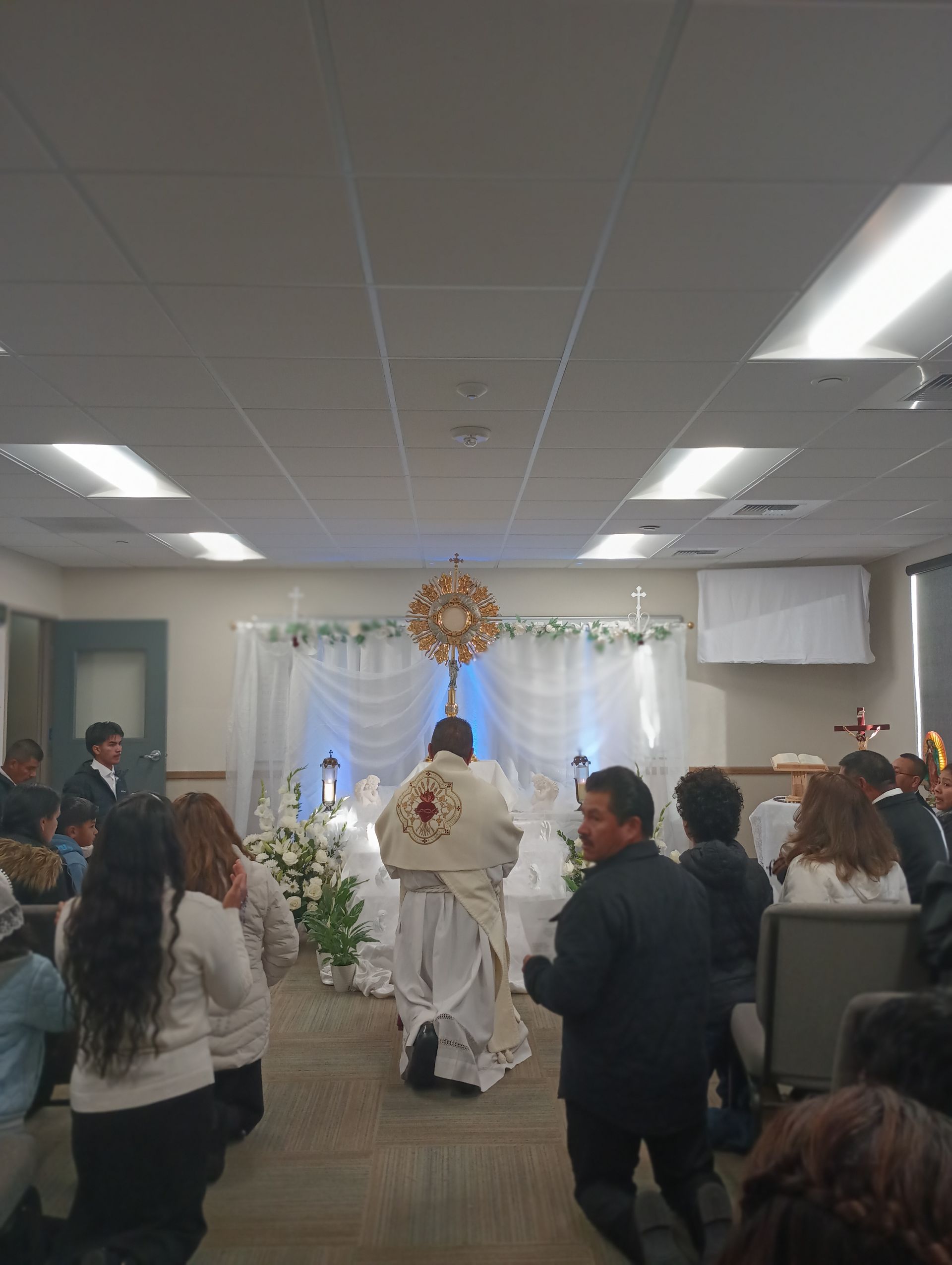 Religious procession in a decorated church hall, with people gathered around a flower-adorned altar.