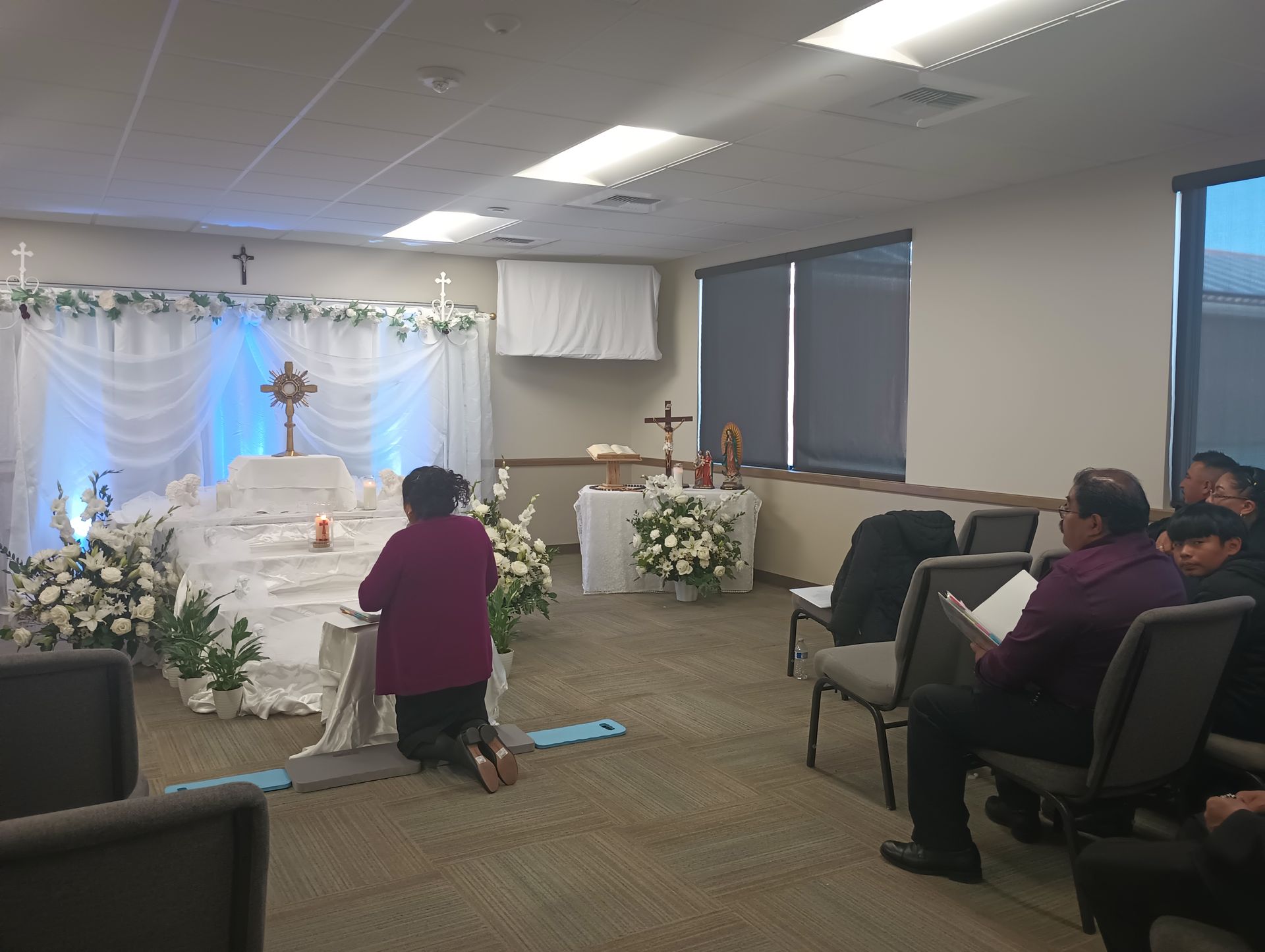 Funeral service room with white casket, floral arrangements, and seated mourners