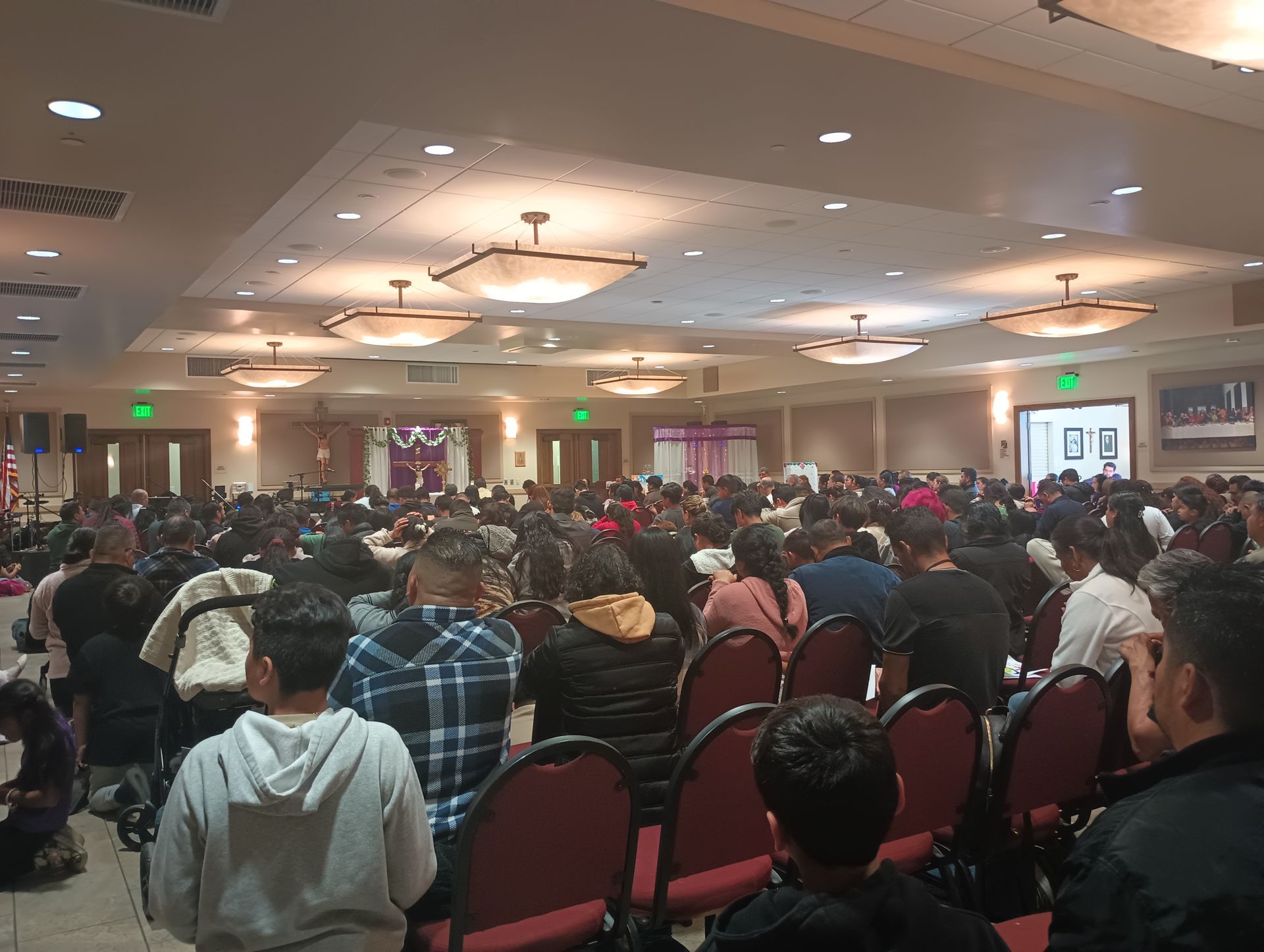 Large conference hall packed with seated attendees facing a presentation screen, under warm ceiling lights.