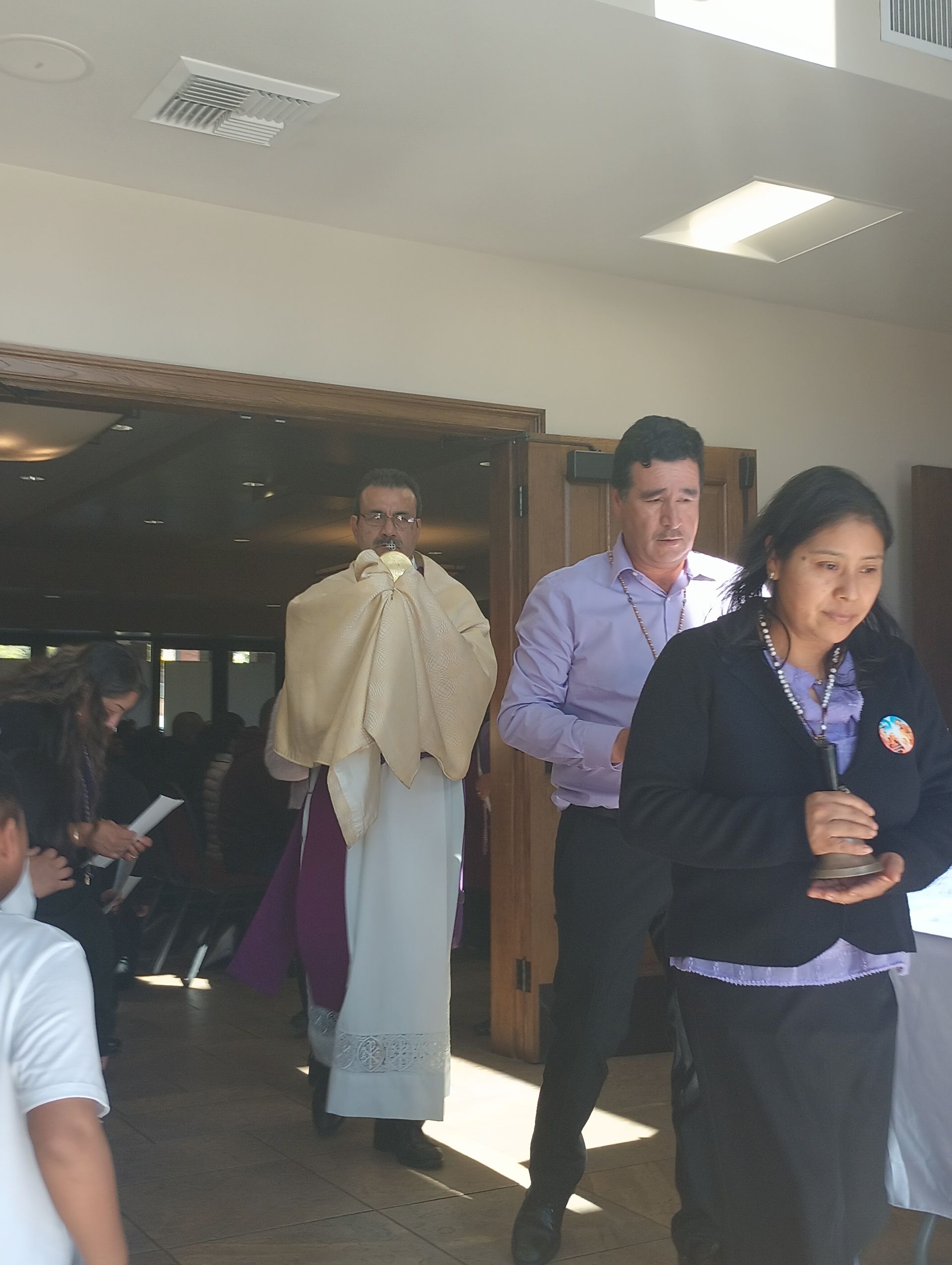 People walking through a doorway indoors, one holding a folded paper fan, with others seated in the background