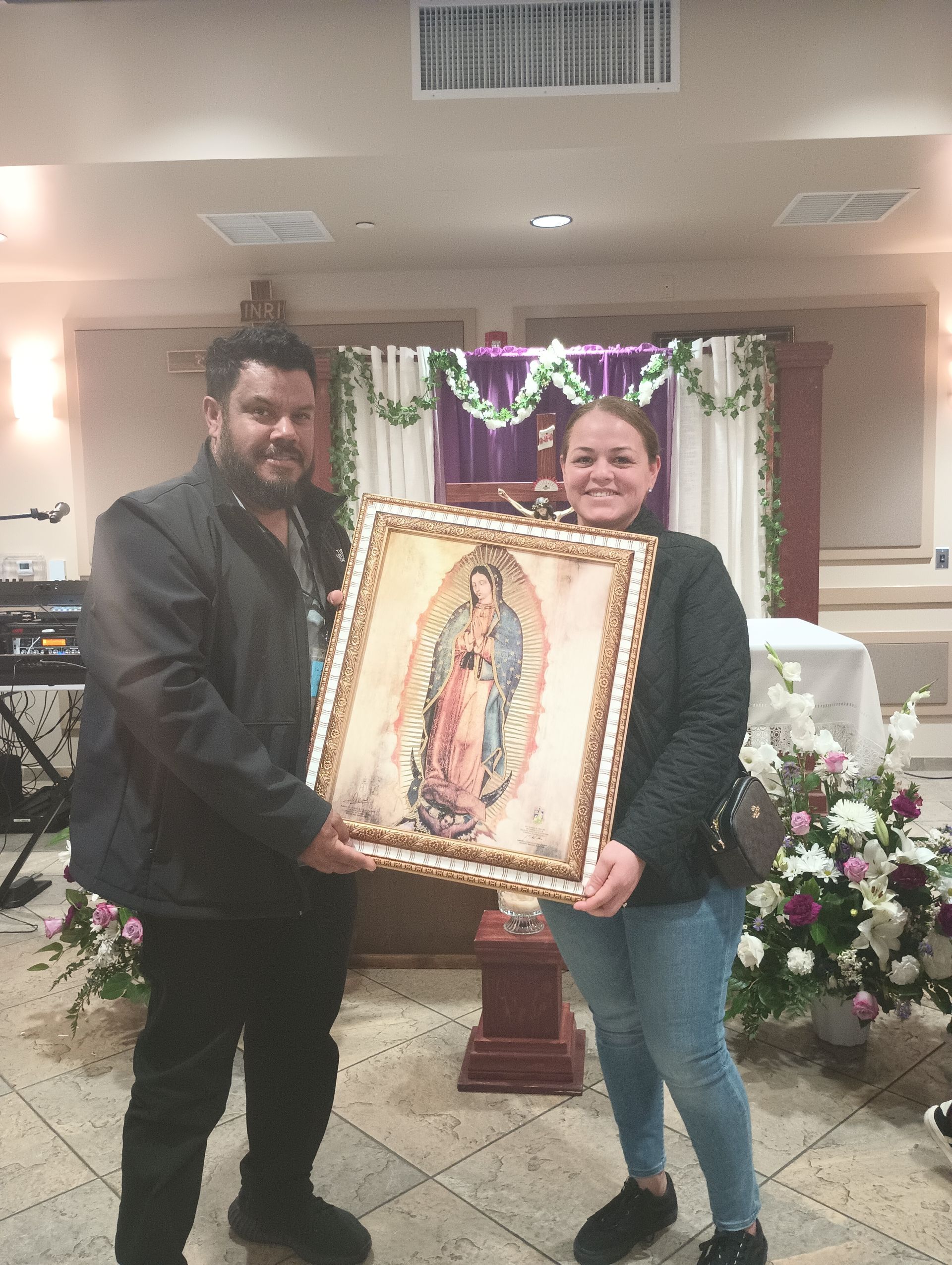 Two people holding a framed picture in a decorated indoor hall