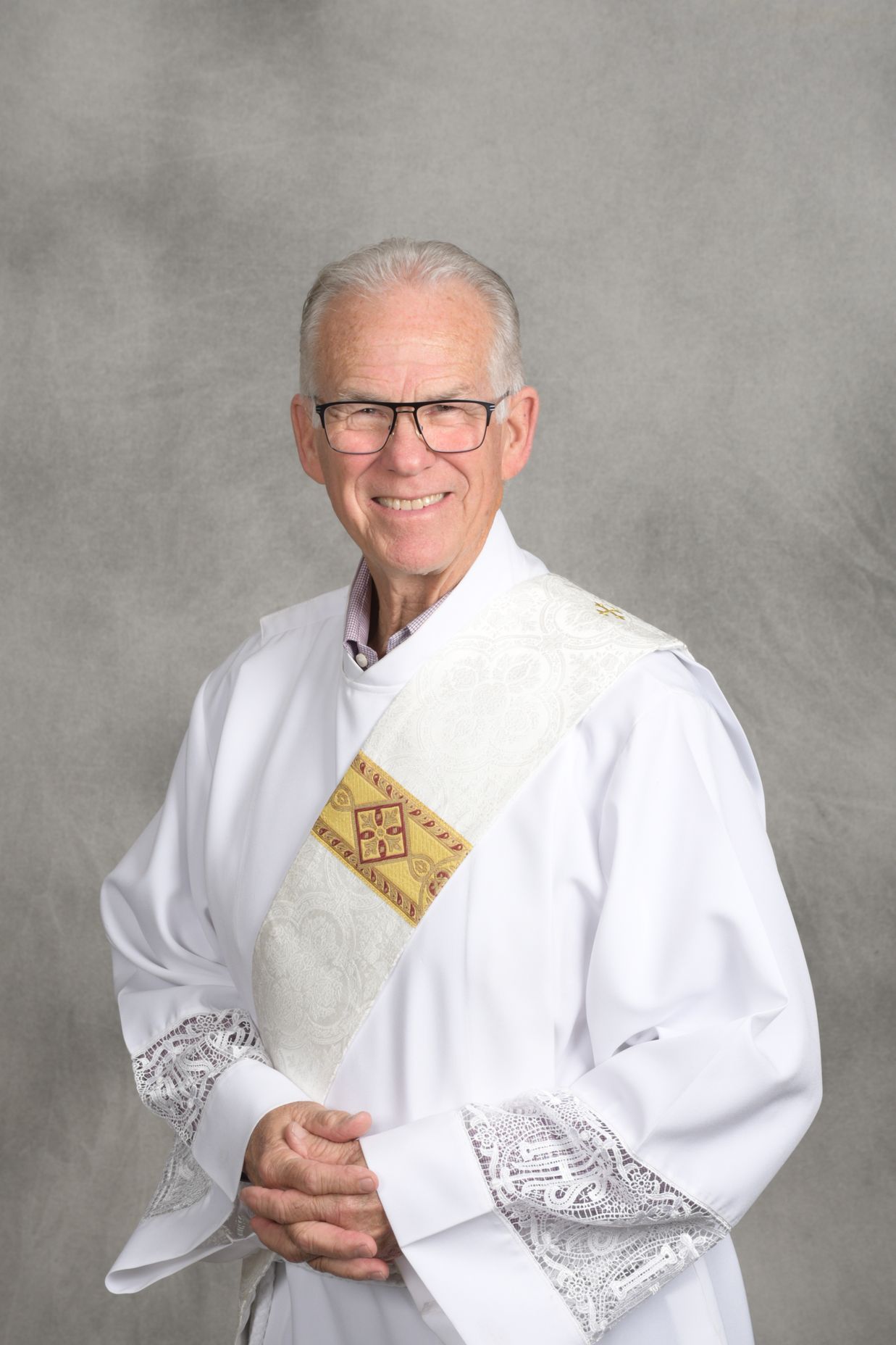Man in white ceremonial robe with gold sash, smiling against a gray studio backdrop