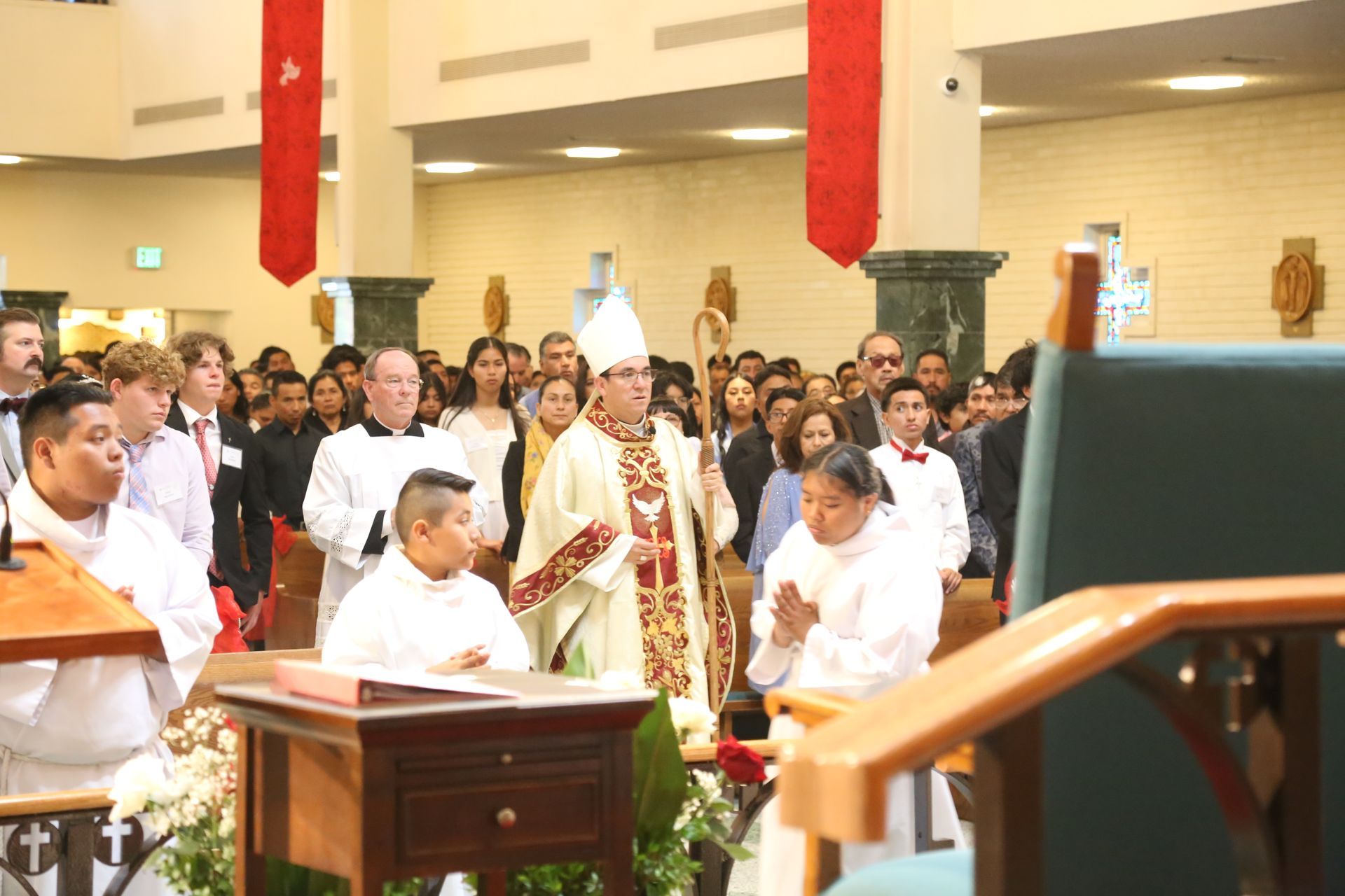 People gathered in a church aisle during a procession, with a child near the front and a lectern in view.