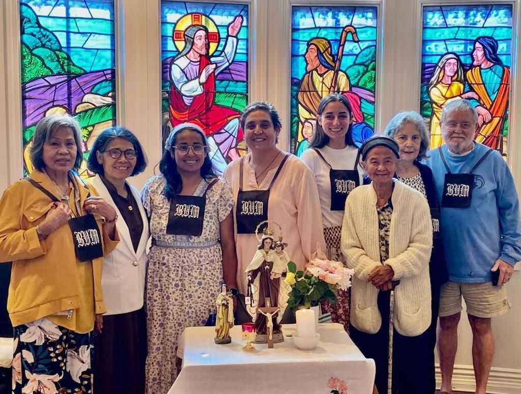 Seven people standing before colorful stained-glass windows, posing behind a small decorated table.