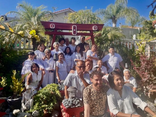 Group of people posing outdoors in a sunny garden with tropical plants and a decorative archway.