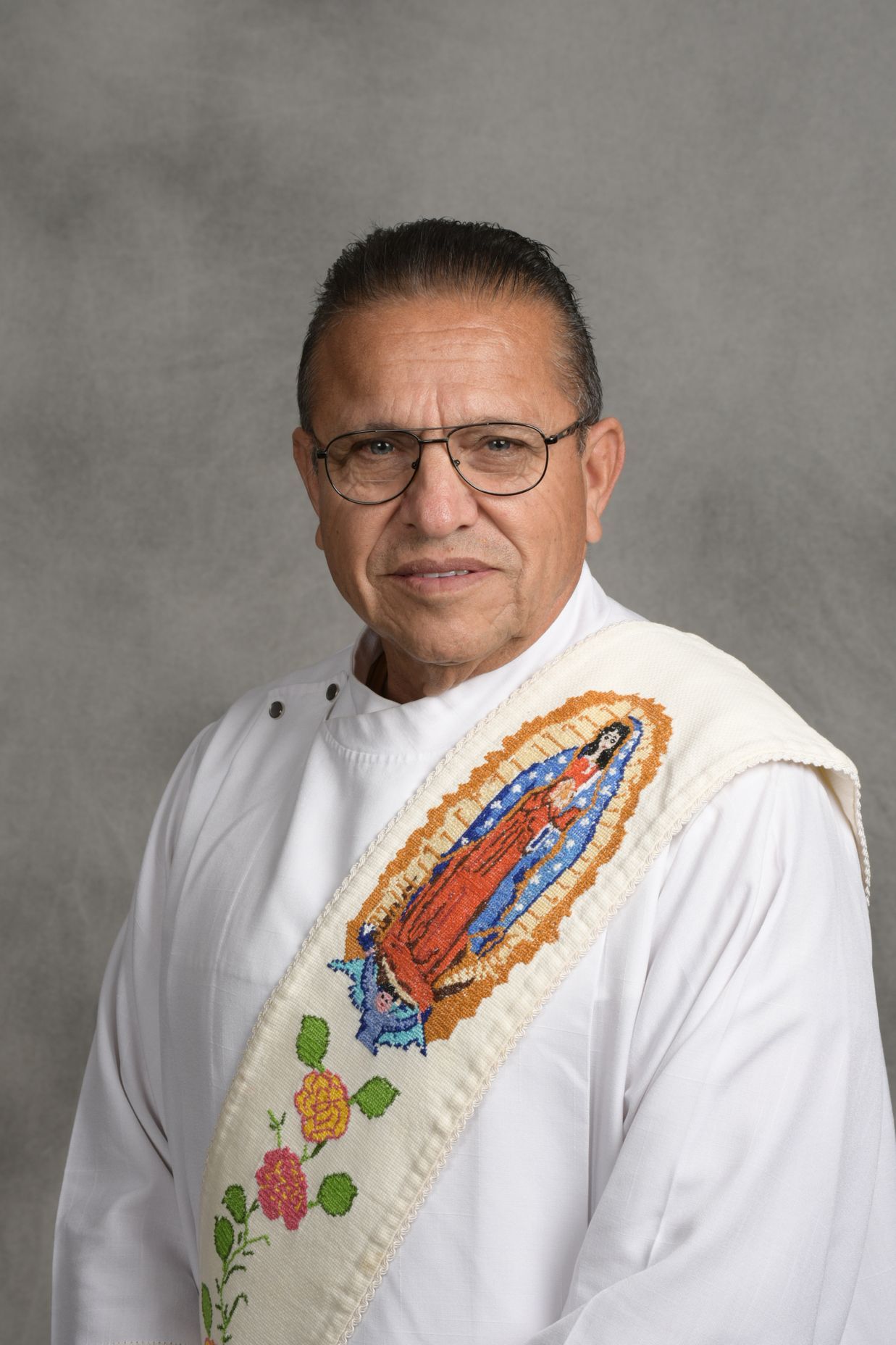 Man in white embroidered shirt with colorful floral design, posing against a gray backdrop.