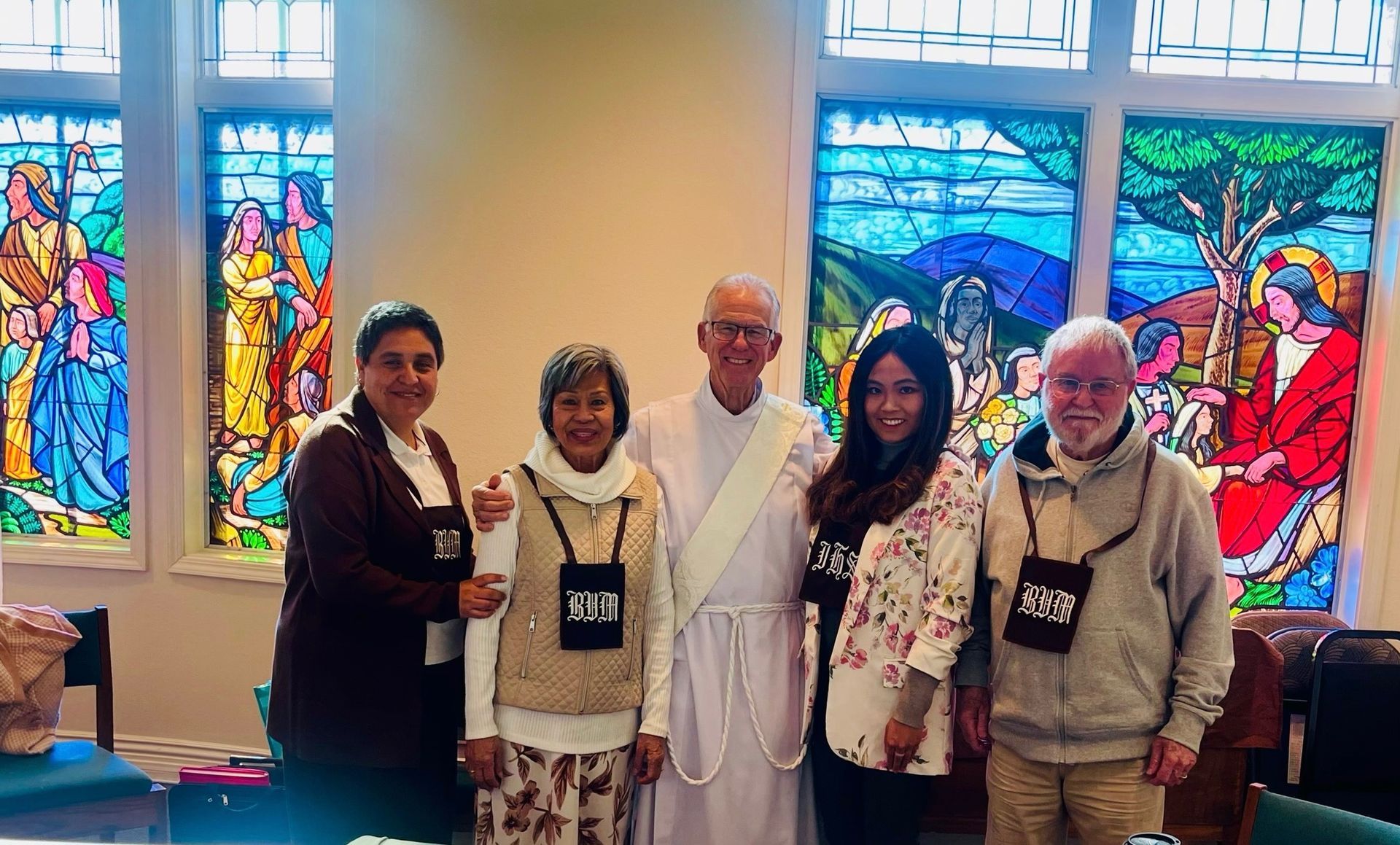 Five people posing in front of colorful stained-glass windows at an indoor event