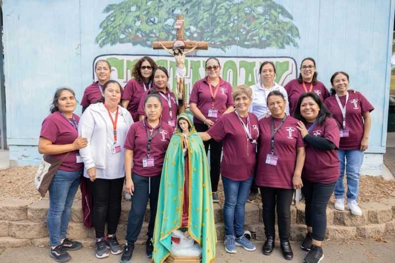 Group of people in maroon shirts posing outdoors in front of a painted mural and sign