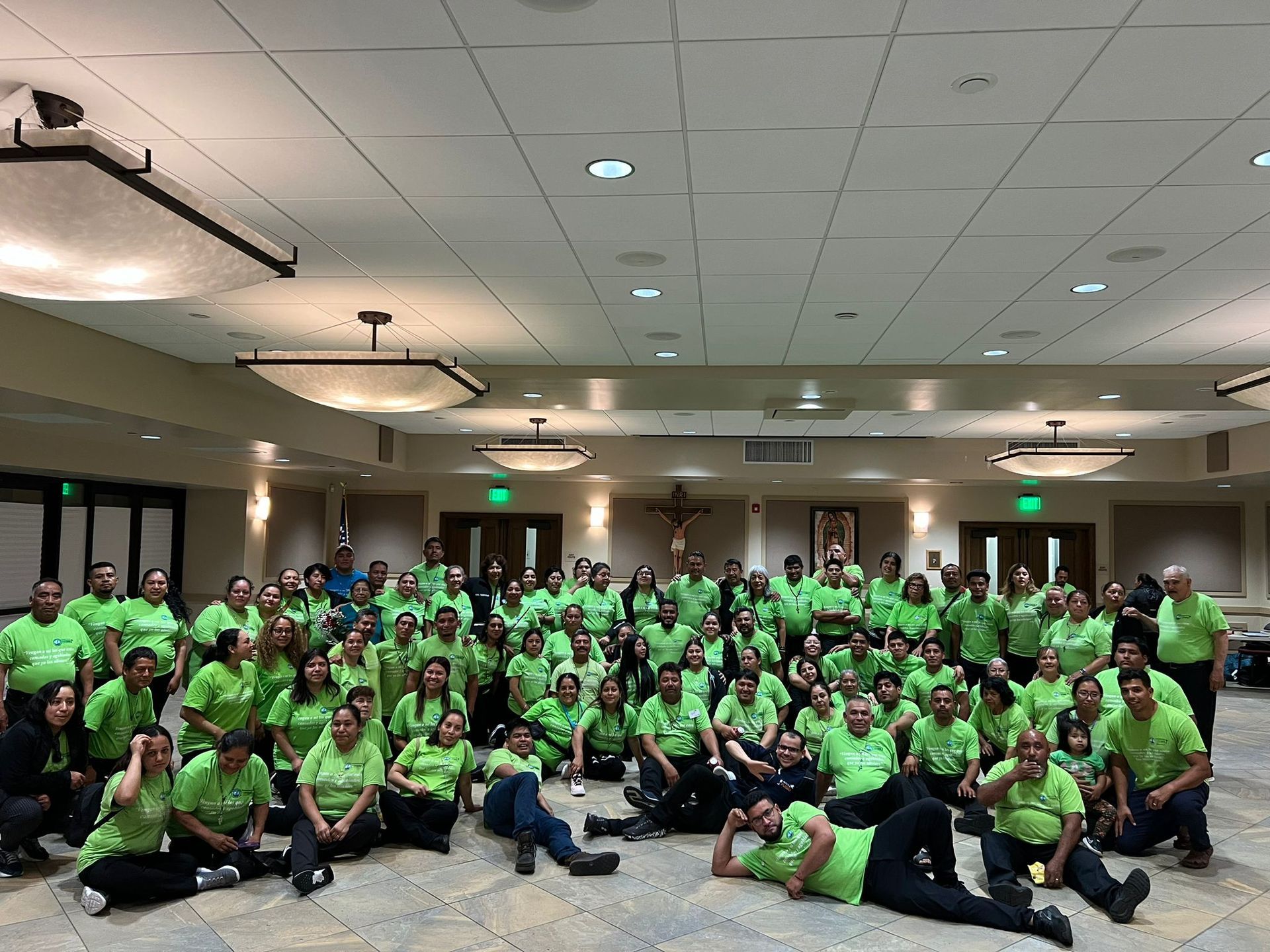 Large group in bright green shirts gathered in a conference room, posing for a group photo.