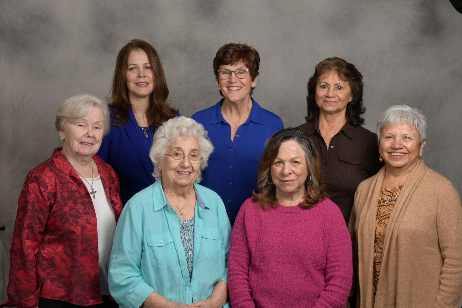 Seven women posing together against a gray studio backdrop.
