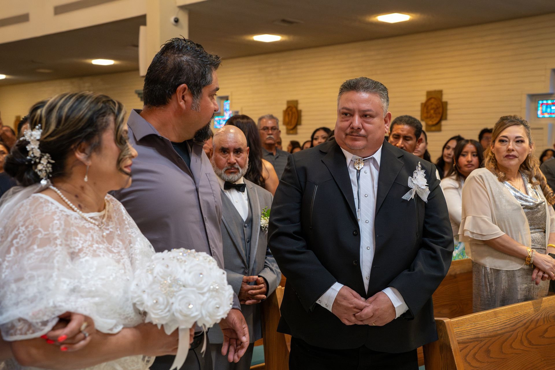 Bride in white lace dress faces guests at an indoor wedding ceremony