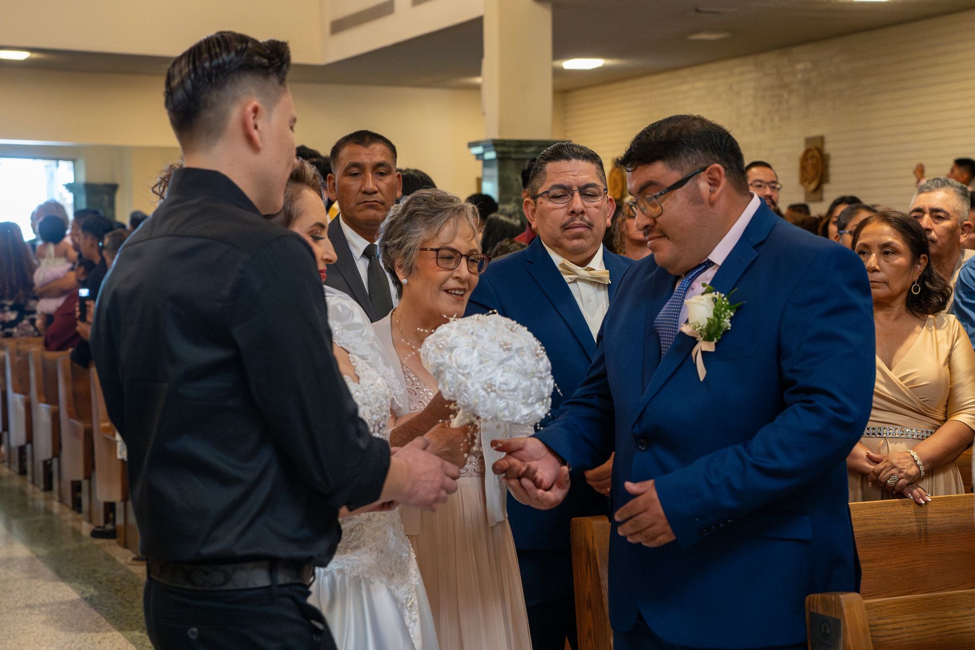 Wedding guests greeting a bride and groom indoors, with the bride holding white flowers.