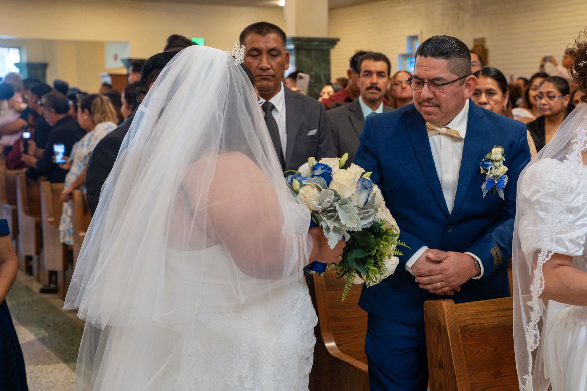Bride in white veil meets groom in blue suit during a church wedding ceremony