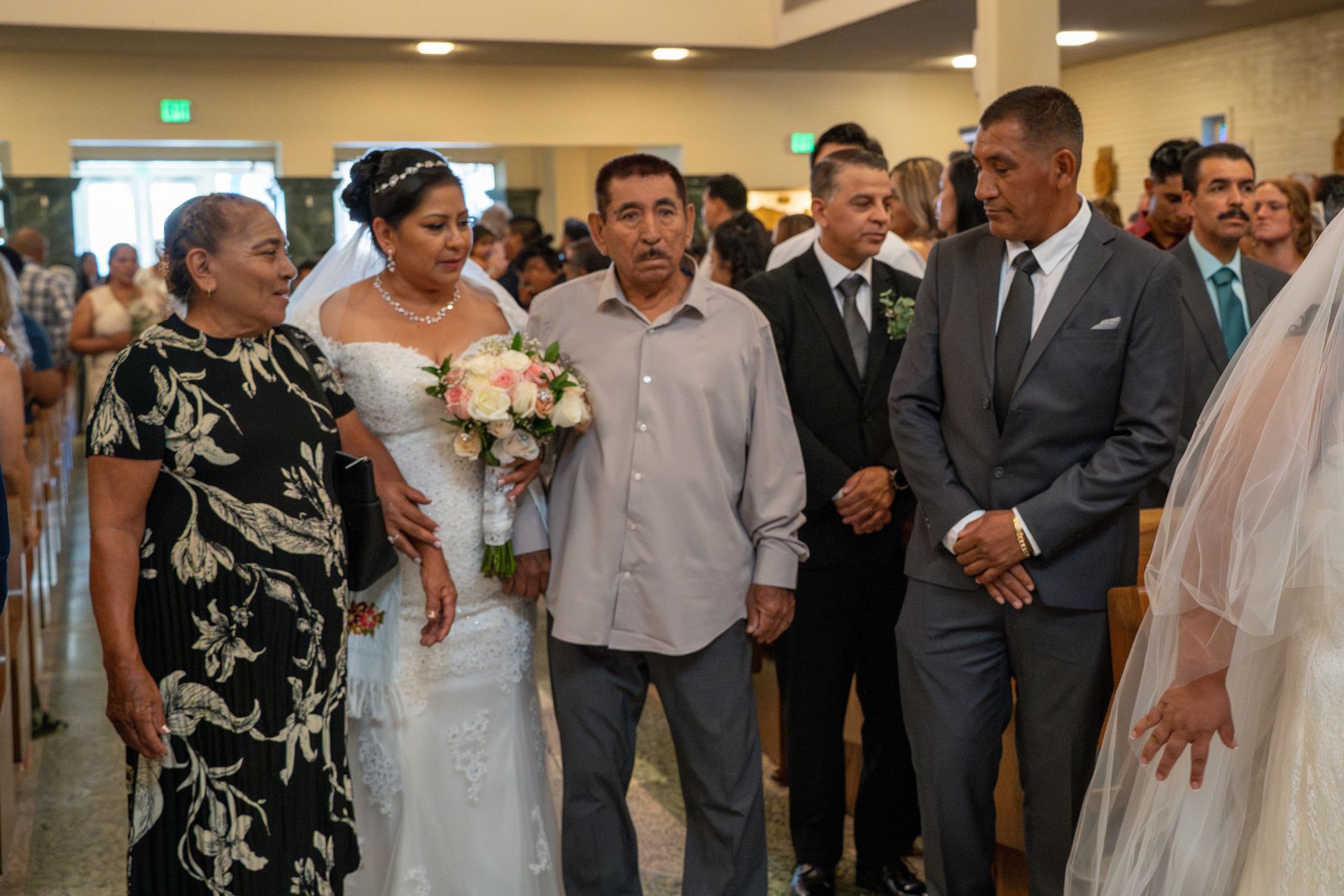 Wedding guests standing indoors beside the bride in a white dress holding a bouquet.