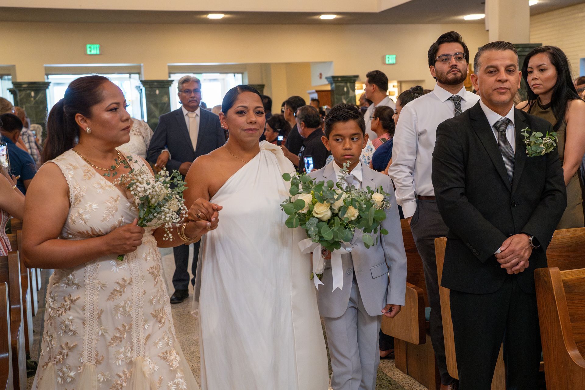 Wedding party walking down aisle with bridesmaids, flower girl, and groom in a church aisle