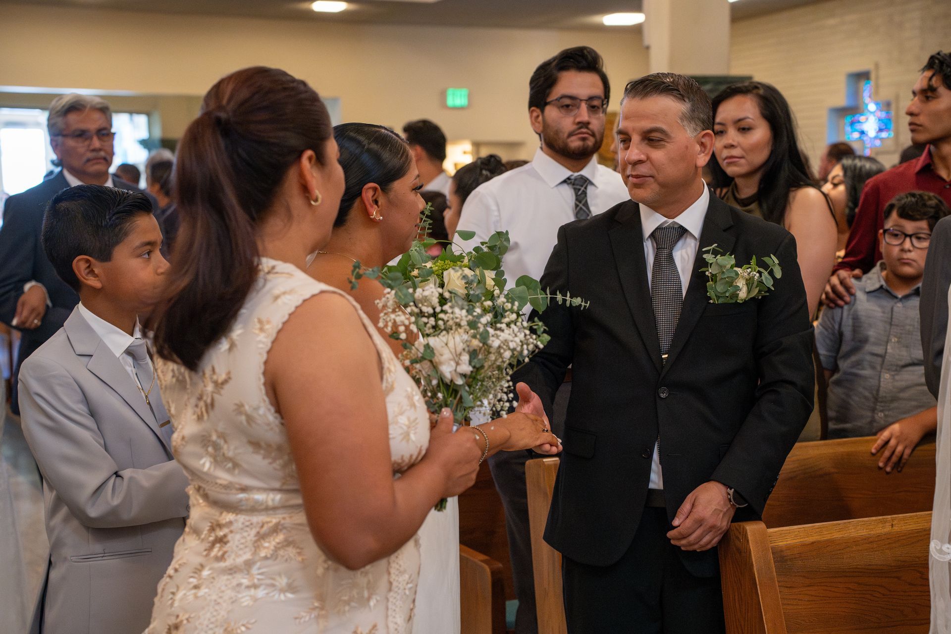Wedding ceremony in a church, with the bride facing the groom as guests watch from the pews.