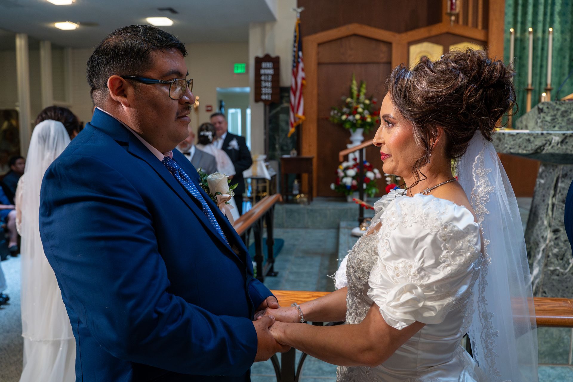 Bride and man in blue suit holding hands during an indoor wedding ceremony
