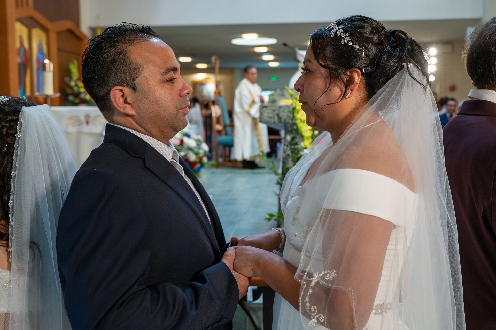 Couple exchanging vows at a wedding ceremony, holding hands in a decorated indoor venue