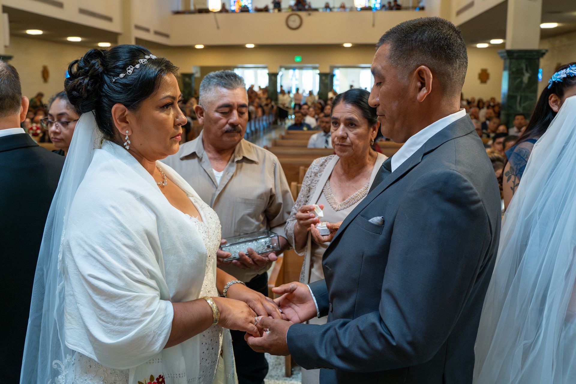 Couple exchanging rings during a church wedding ceremony, with guests watching nearby.