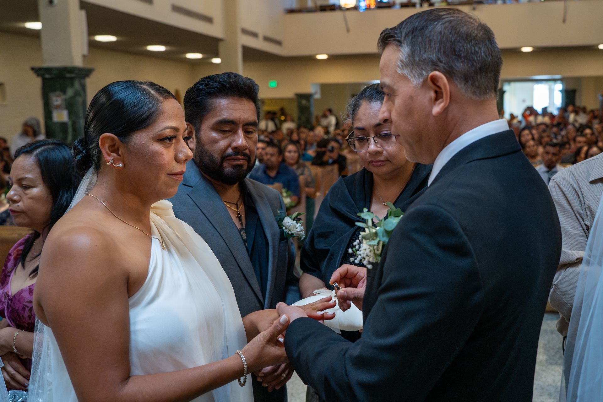 Wedding ceremony with bride and groom exchanging rings before guests in a bright hall