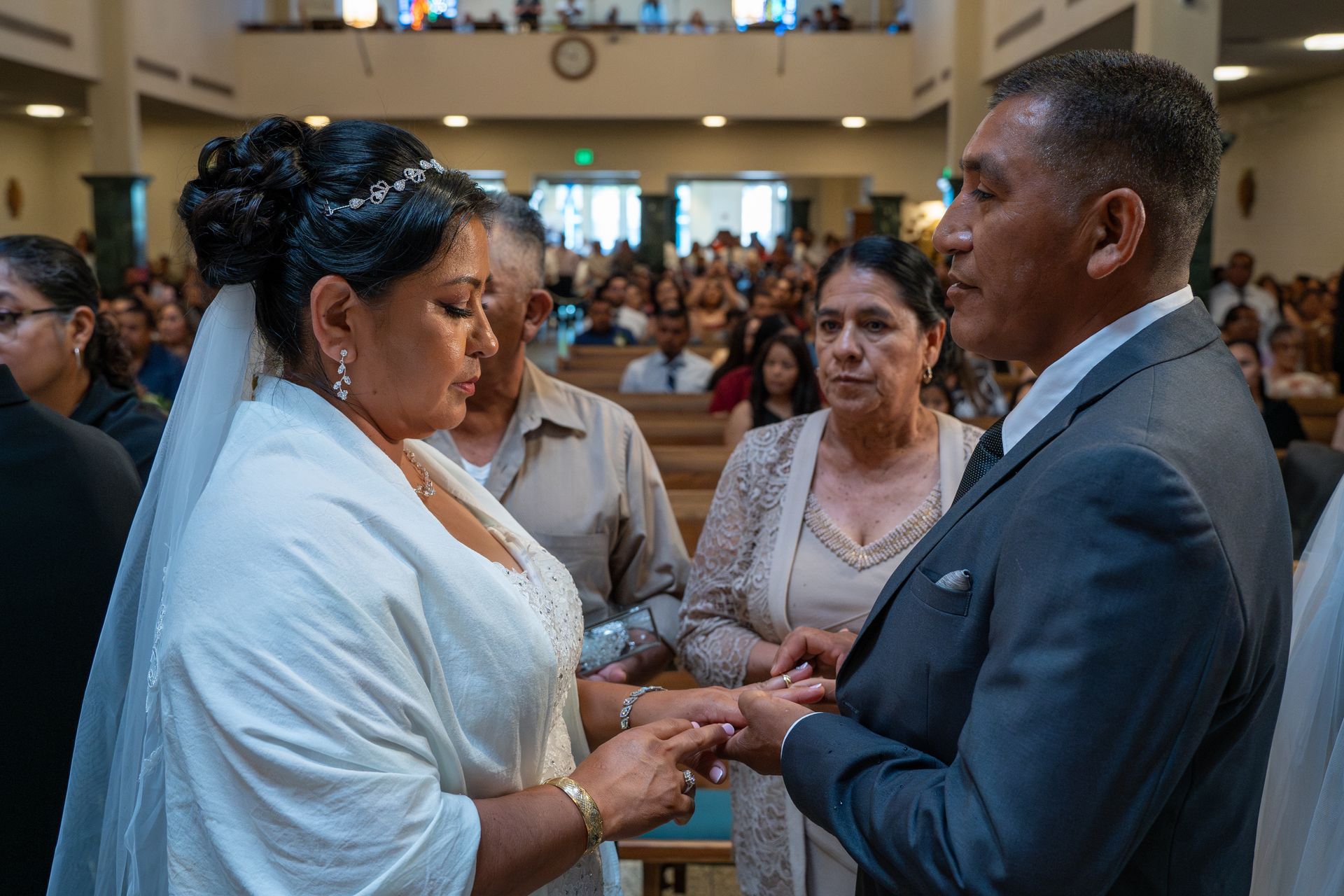 Couple holding hands during a wedding ceremony in a church, with guests seated behind them.