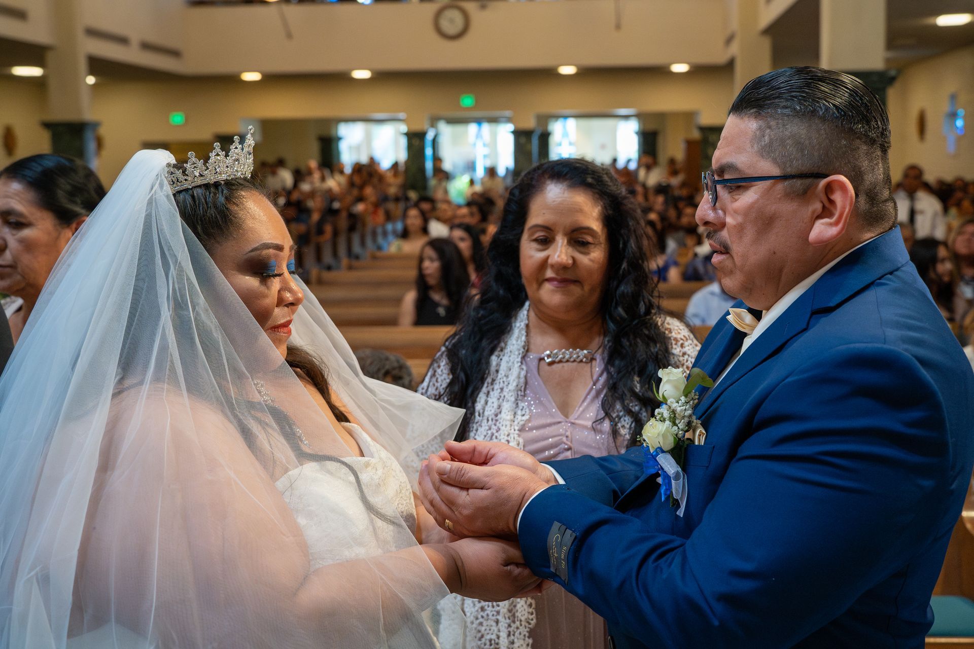 Bride and groom exchanging rings during a wedding ceremony in a church, with guests seated behind them.