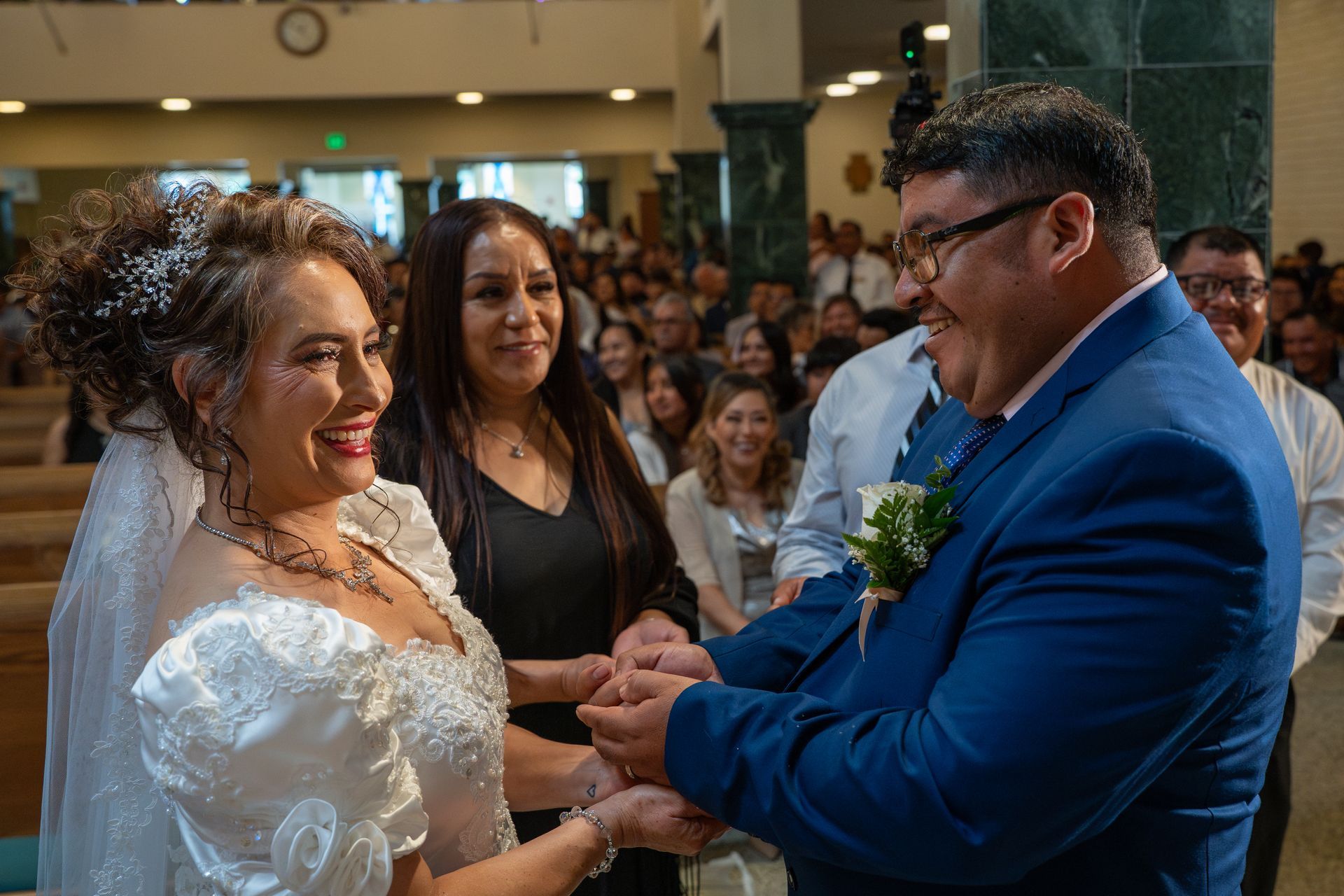 Bride smiling and holding hands with a man in a blue suit during a wedding ceremony indoors