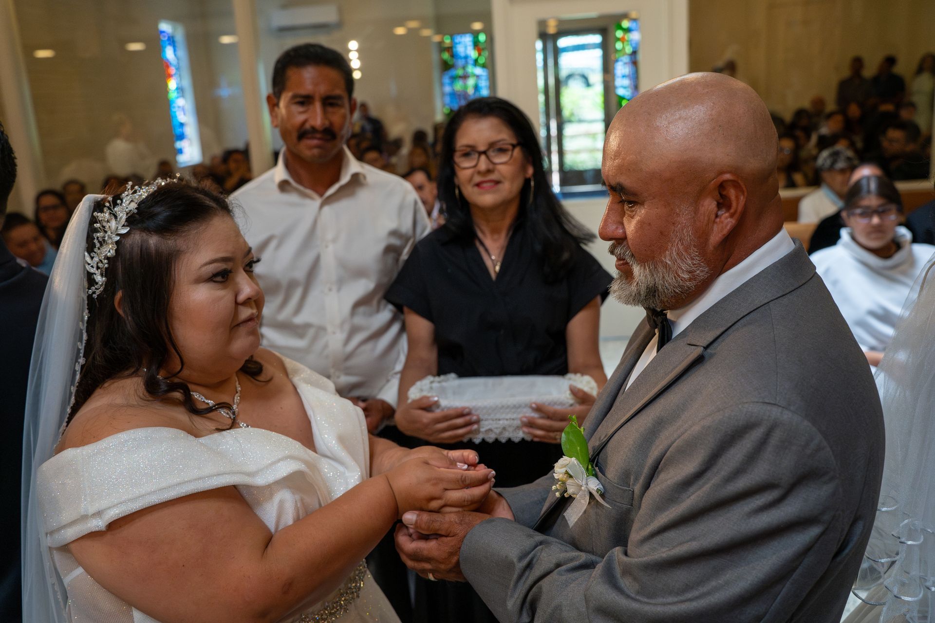 Wedding couple holding hands in a church during a ceremony, with guests seated in the background.