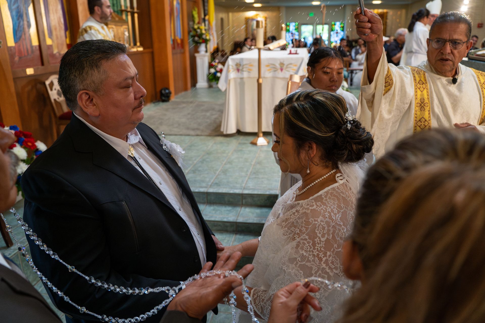 Couple exchanging rings during a church wedding ceremony, with a priest in the background