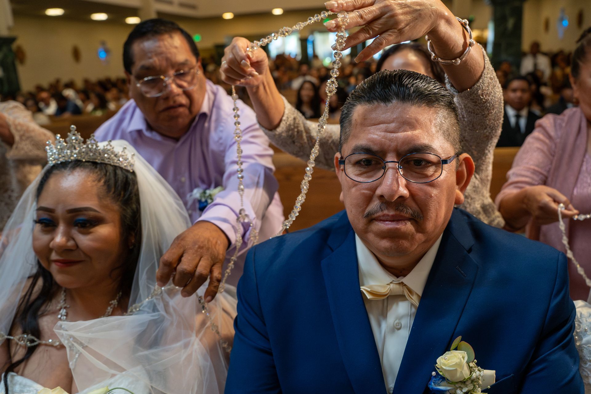 Wedding guests placing crowns on a seated bride and groom during a ceremony