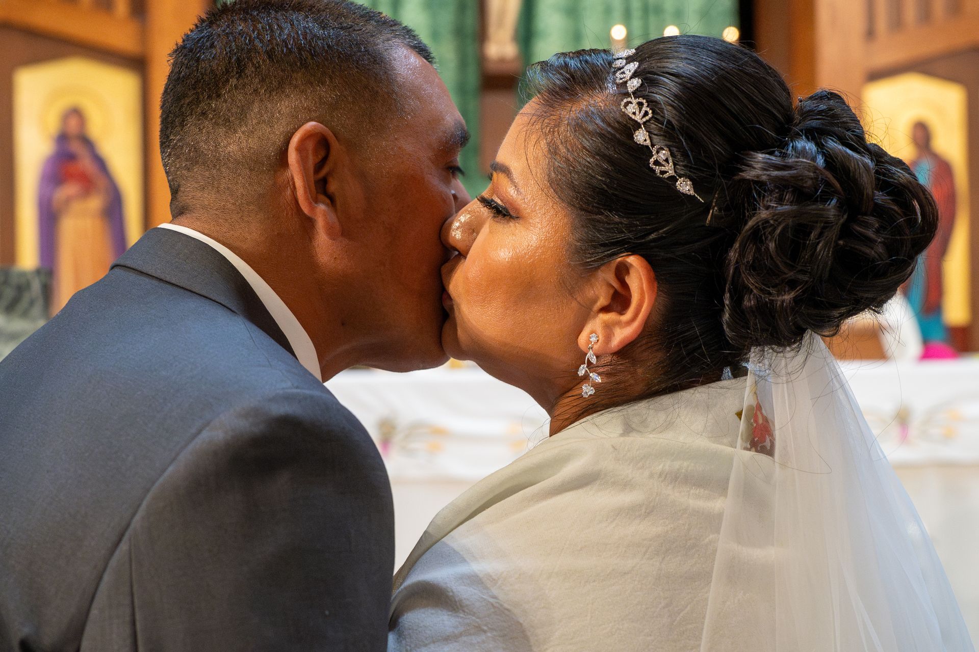 Couple kissing during a wedding ceremony, with the bride’s veil and floral hairpiece visible.