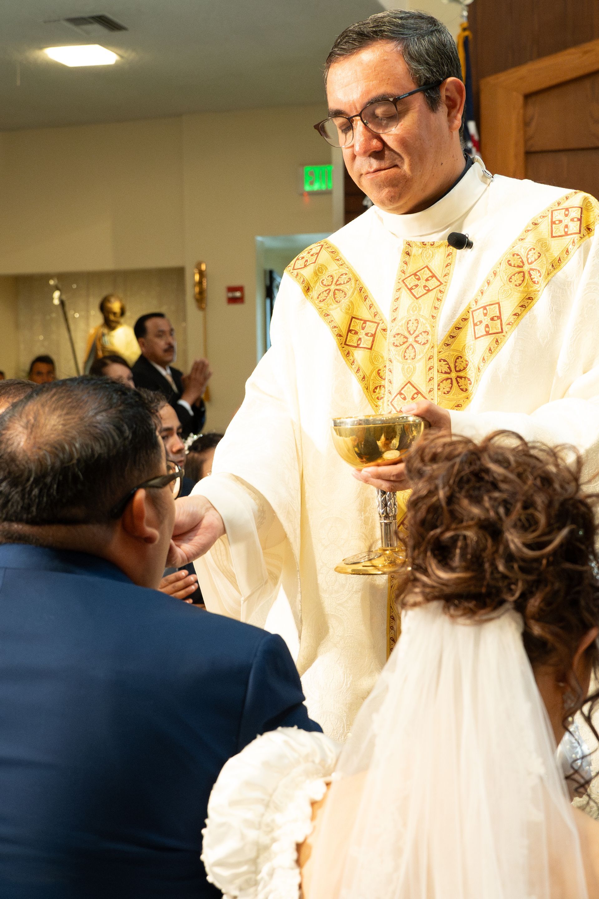 Priest in white and gold vestments blessing a bride and groom during a wedding ceremony