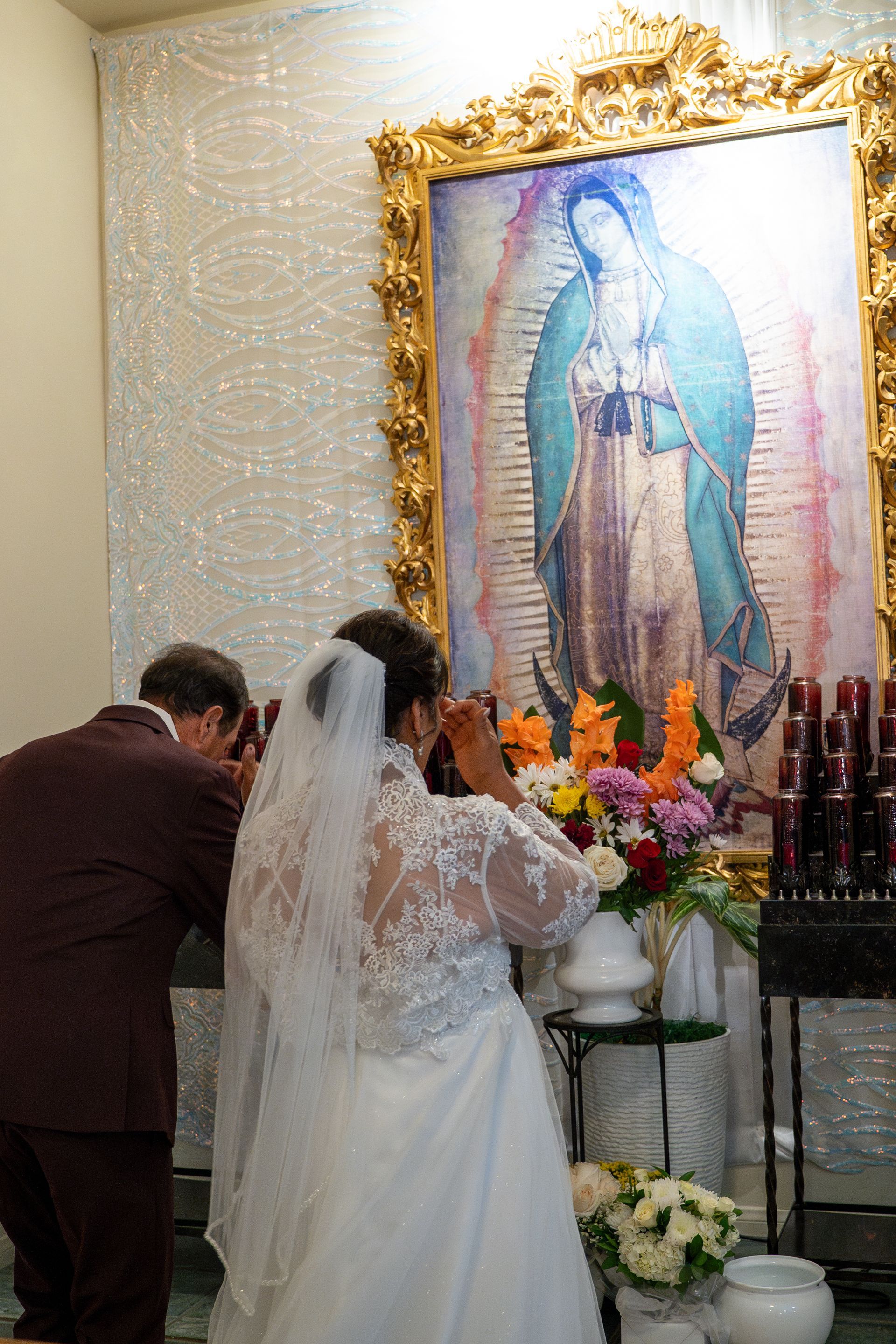 Bride and groom praying before a framed image of the Virgin Mary at an altar