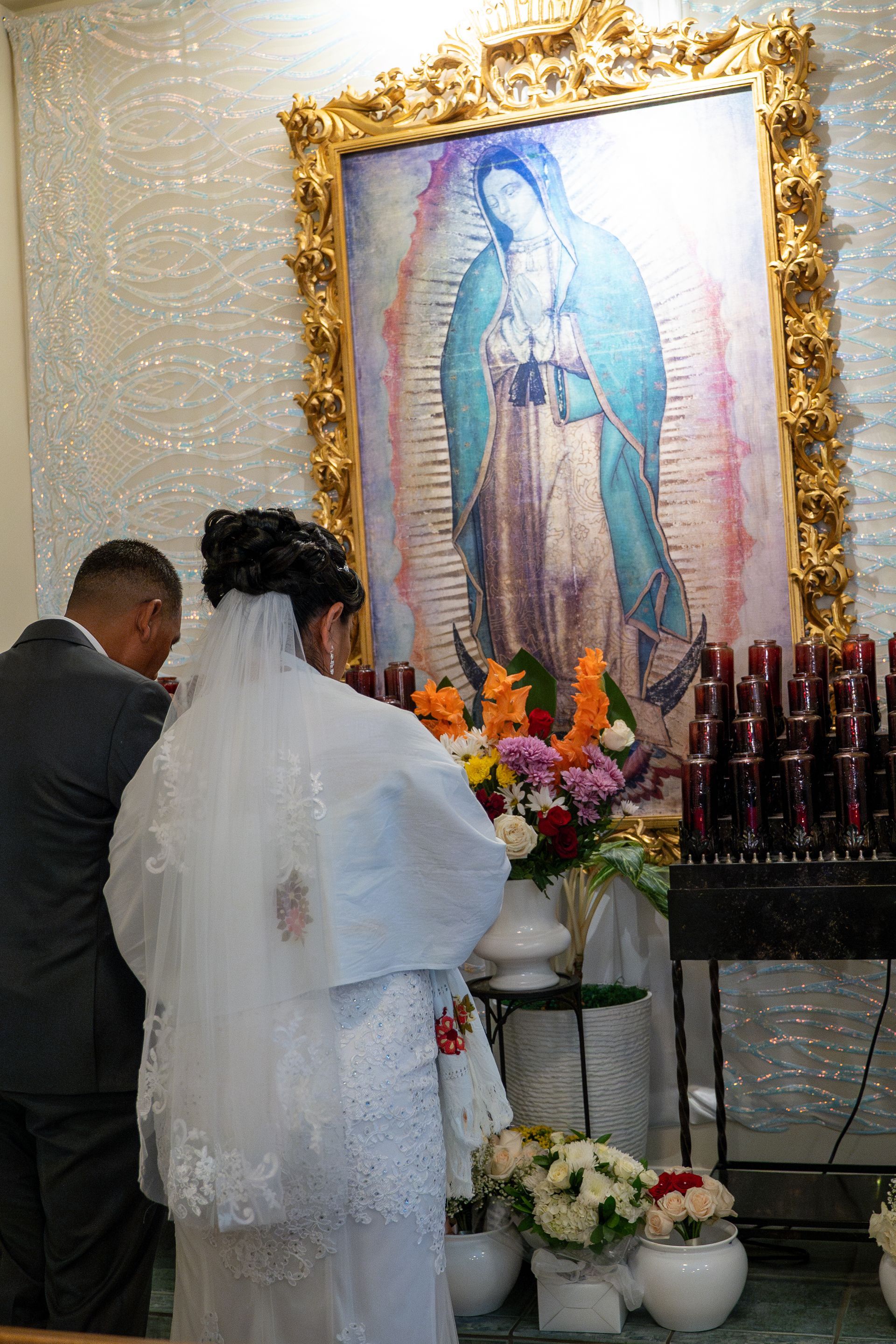 Wedding couple standing before framed Virgin Mary altar with flowers and candles