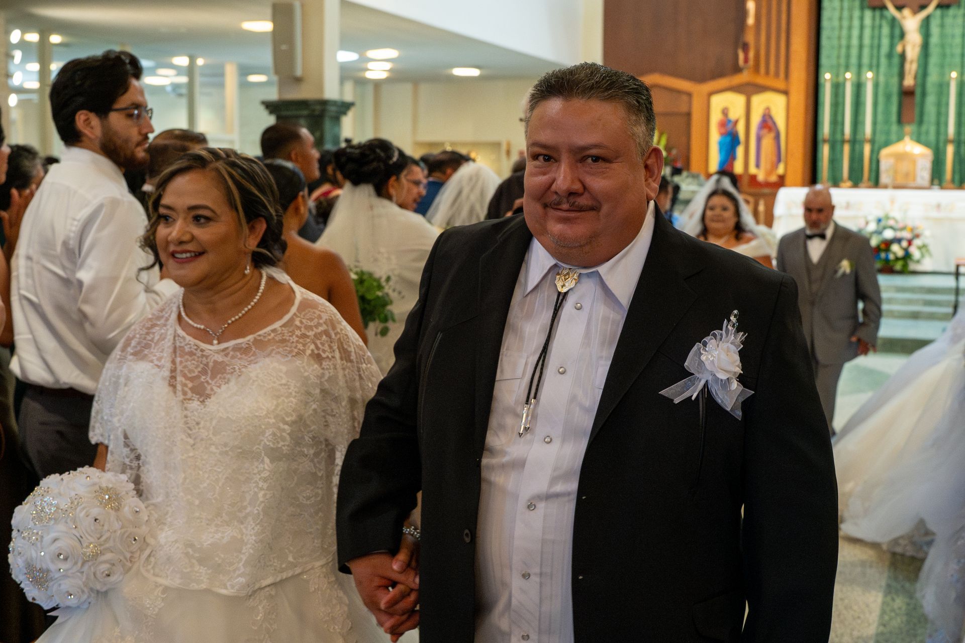 Couple in wedding attire walking together in a church aisle, smiling and holding hands