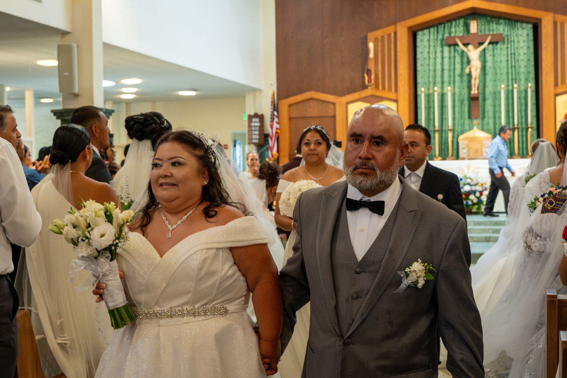 Wedding couple walking down the aisle in a church, with guests and a crucifix in the background