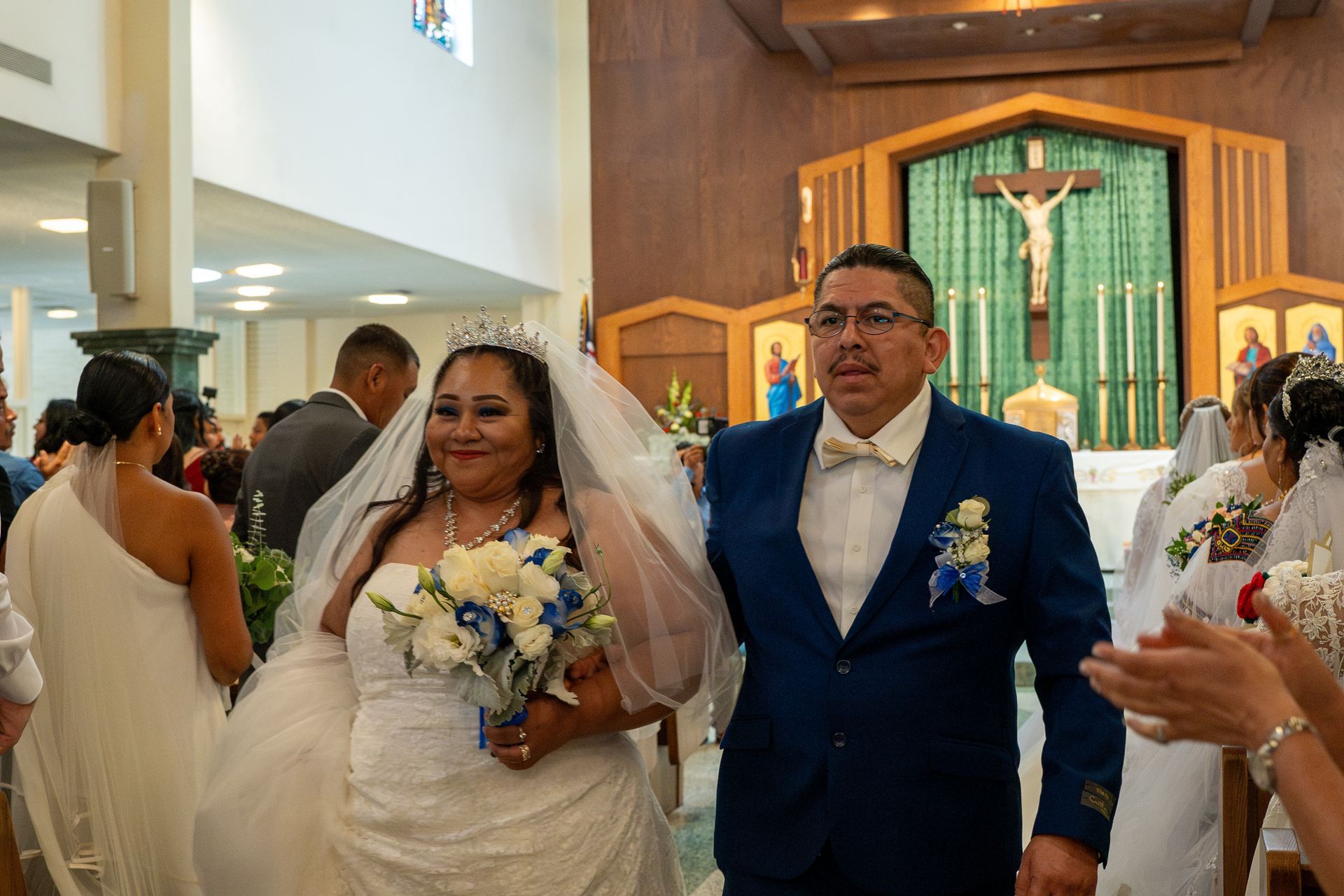 Bride and groom walking down church aisle, bride holding bouquet, altar with crucifix in background