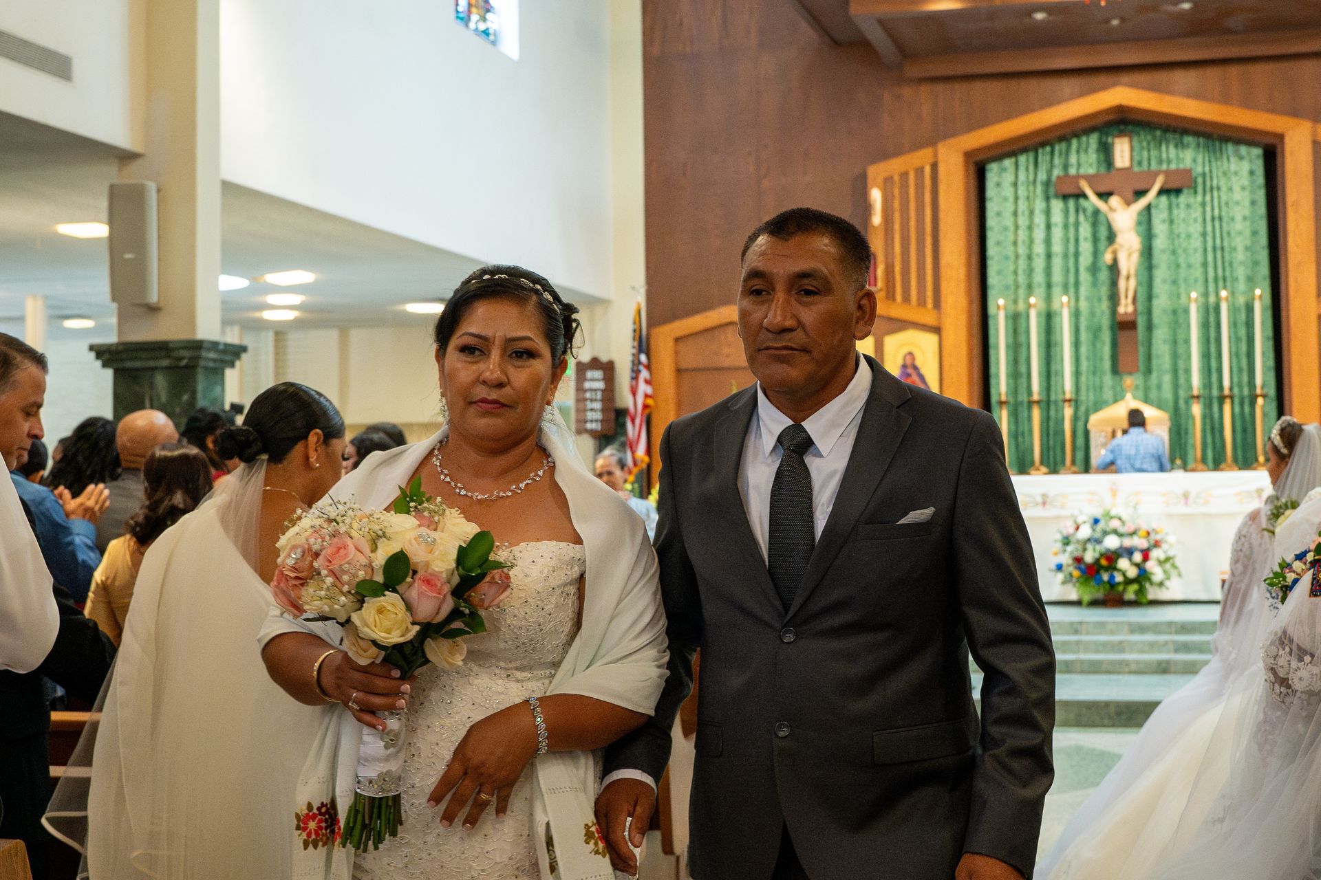 Bride and groom standing in a church aisle, the bride holding a bouquet and wearing a white dress.