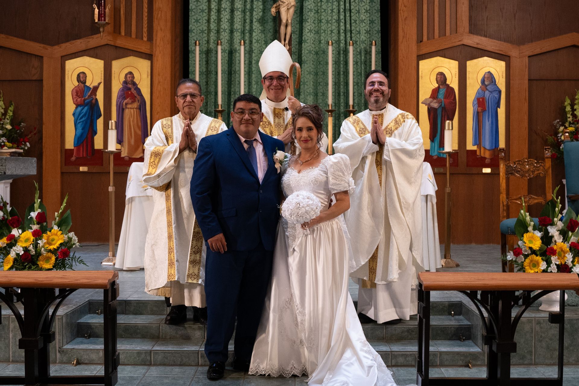 Wedding couple posing with officiants inside a church, with a white gown and dark suit at the altar.