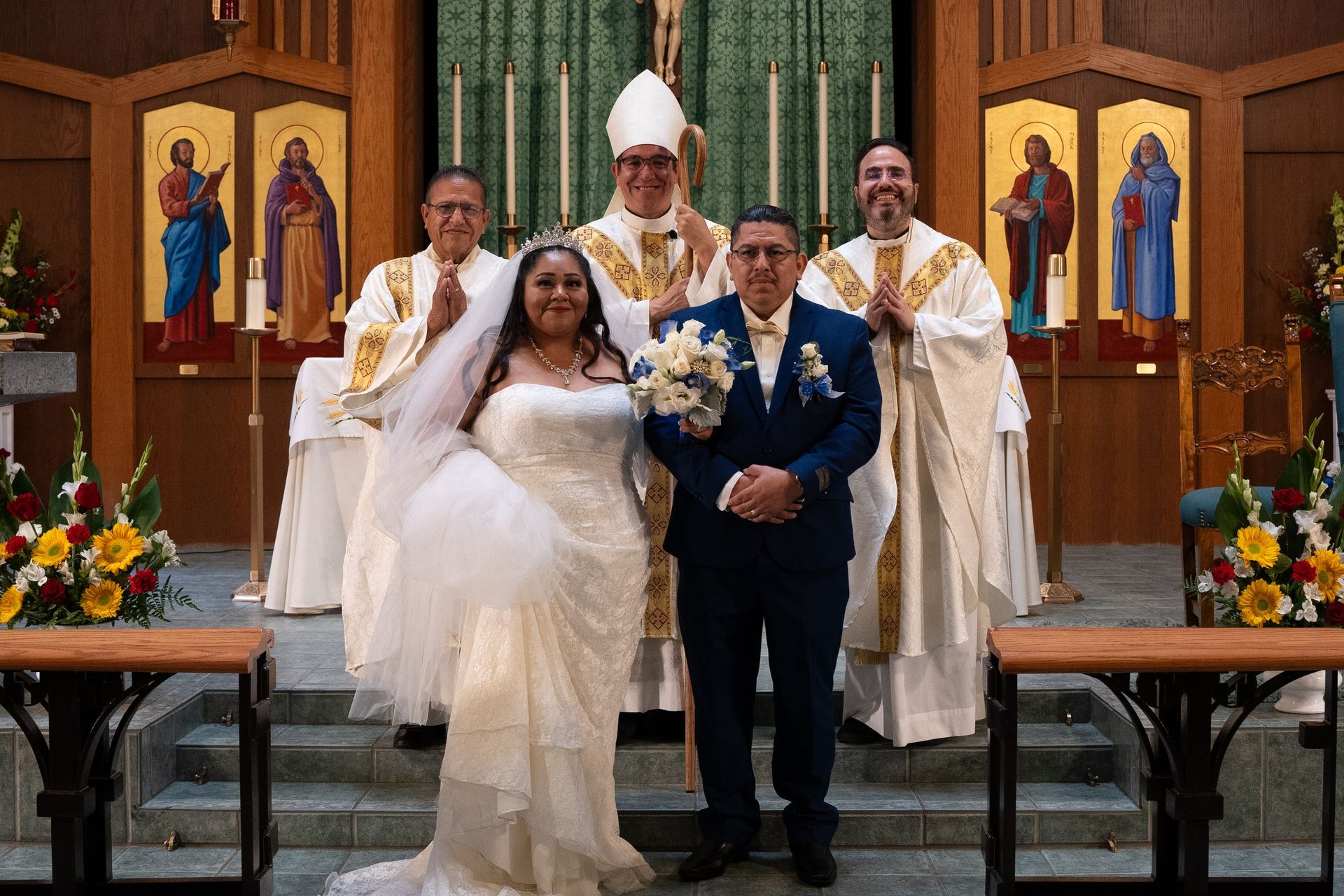 Wedding couple posing with officiants inside a church, bride in white and groom in navy suit holding bouquet.