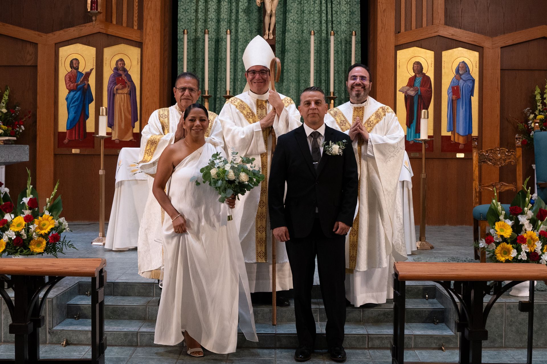 Wedding party posing in a church, with bride, groom, and clergy at the altar.