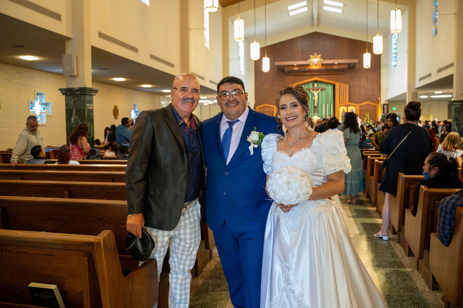 Three people pose in a church aisle during a wedding ceremony