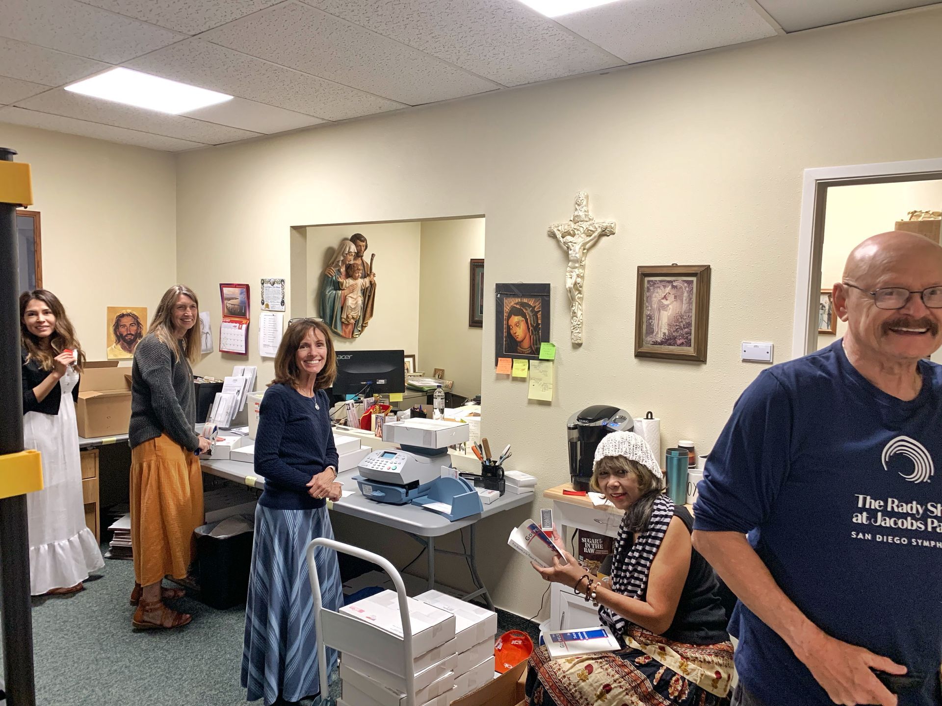 People gathered in an office, with one person seated at a desk and others standing nearby, smiling.