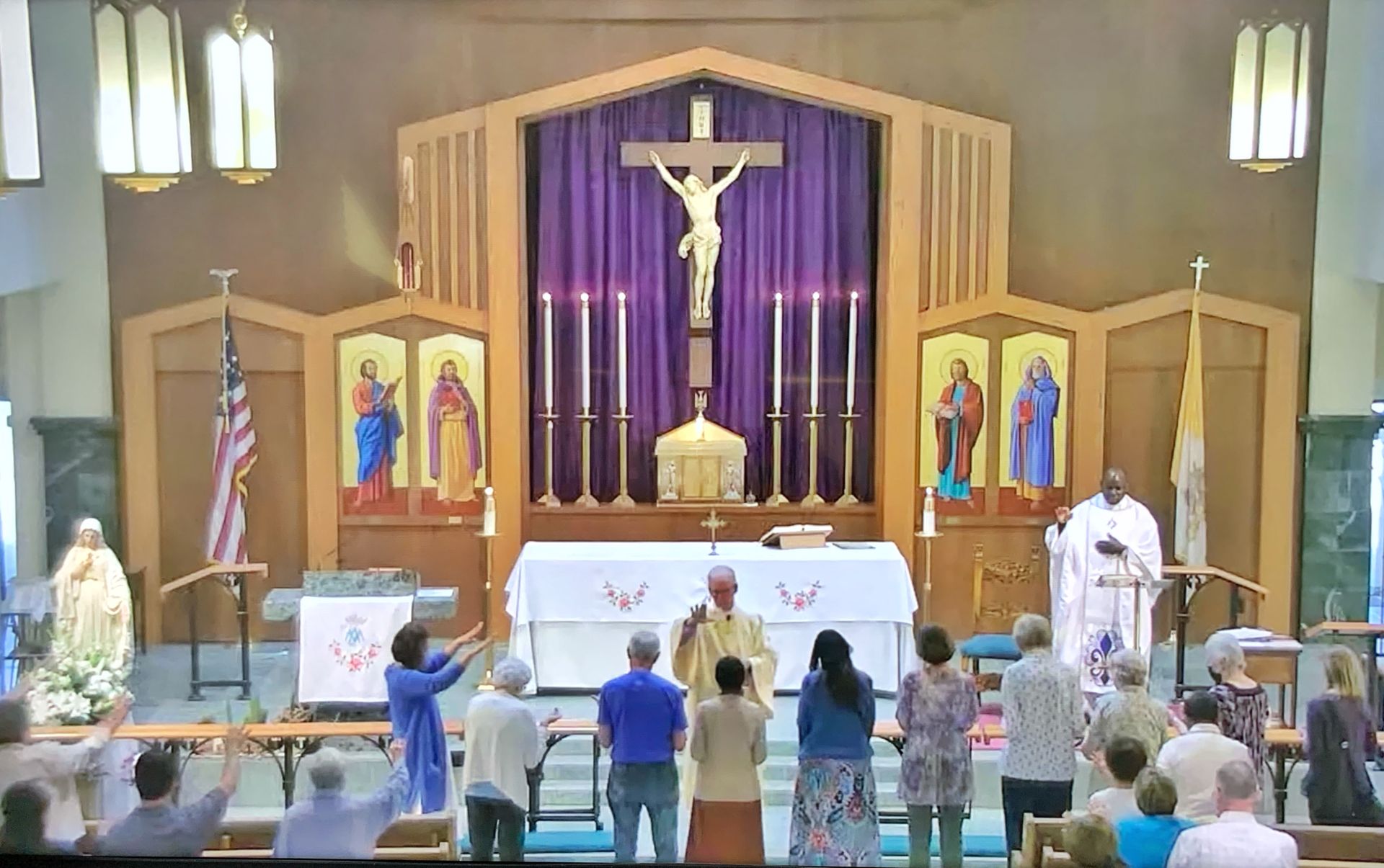 Church sanctuary with altar and crucifix, priest at front, congregants standing in pews during service