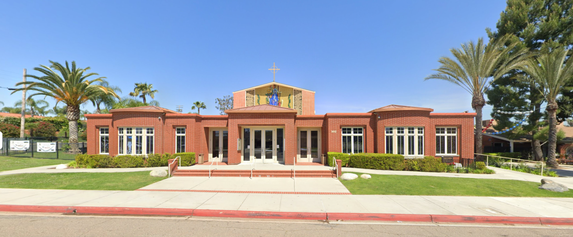 Front view of a red-brick civic building with white columns and palm trees under a clear blue sky