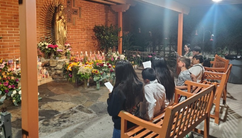 People seated on wooden benches at a flower-lit outdoor brick patio at night