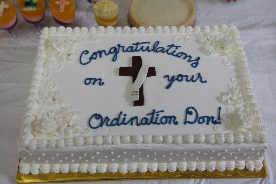 White cake with blue icing reads “Congratulations on your Ordination Don!”