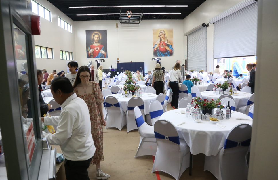 Banquet hall with round tables dressed in white and blue, guests mingling under bright lights