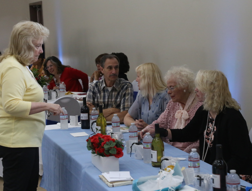 People seated at a meeting table while a woman stands speaking beside them