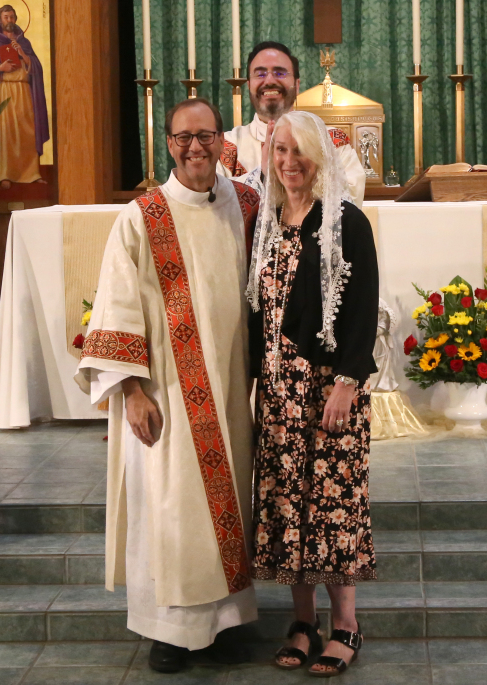Three people posing at a church altar, with flowers and candles behind them.